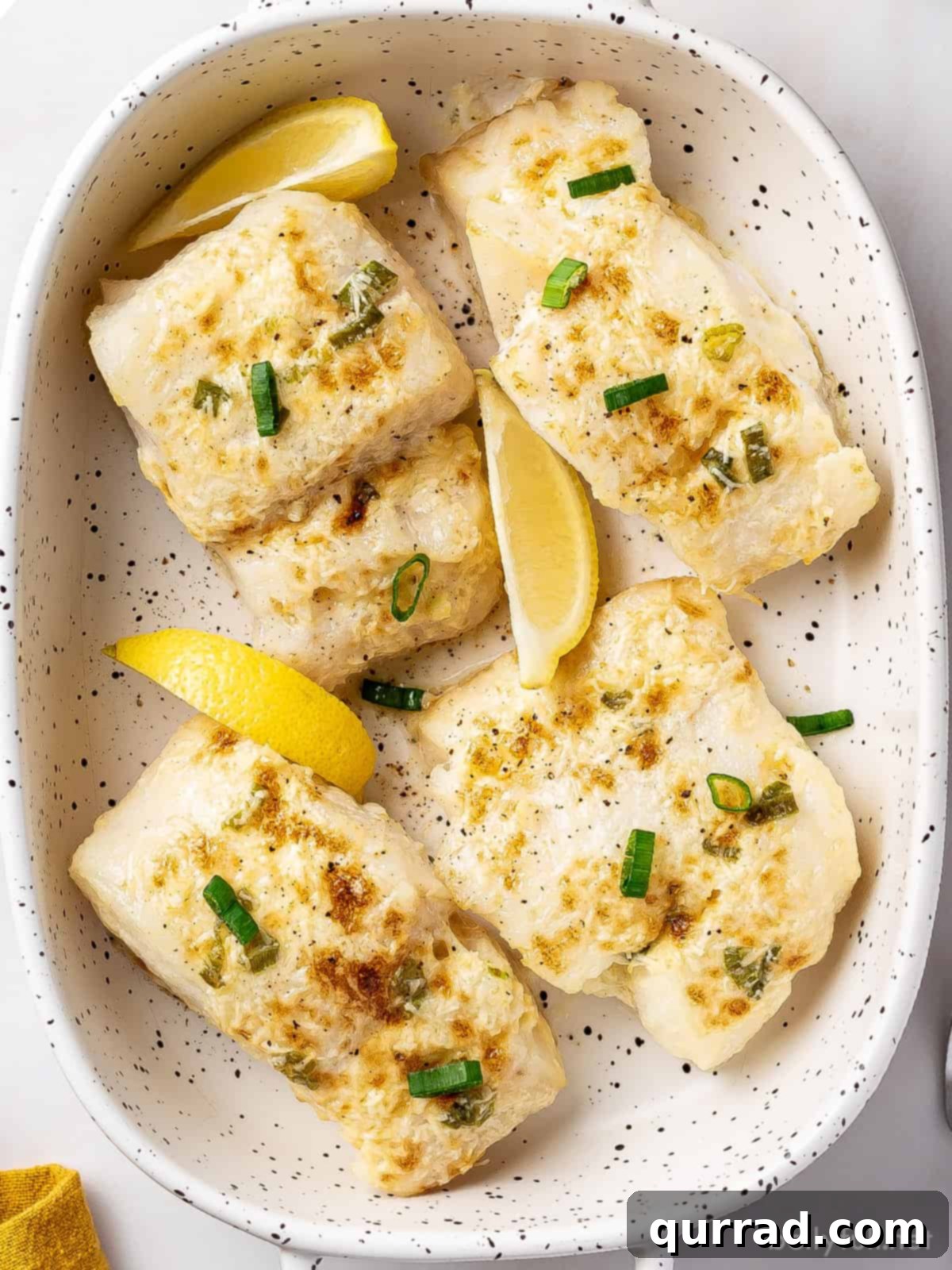 Overhead view of several baked halibut fillets topped with fresh lemon wedges and vibrant diced scallions, ready to be served.