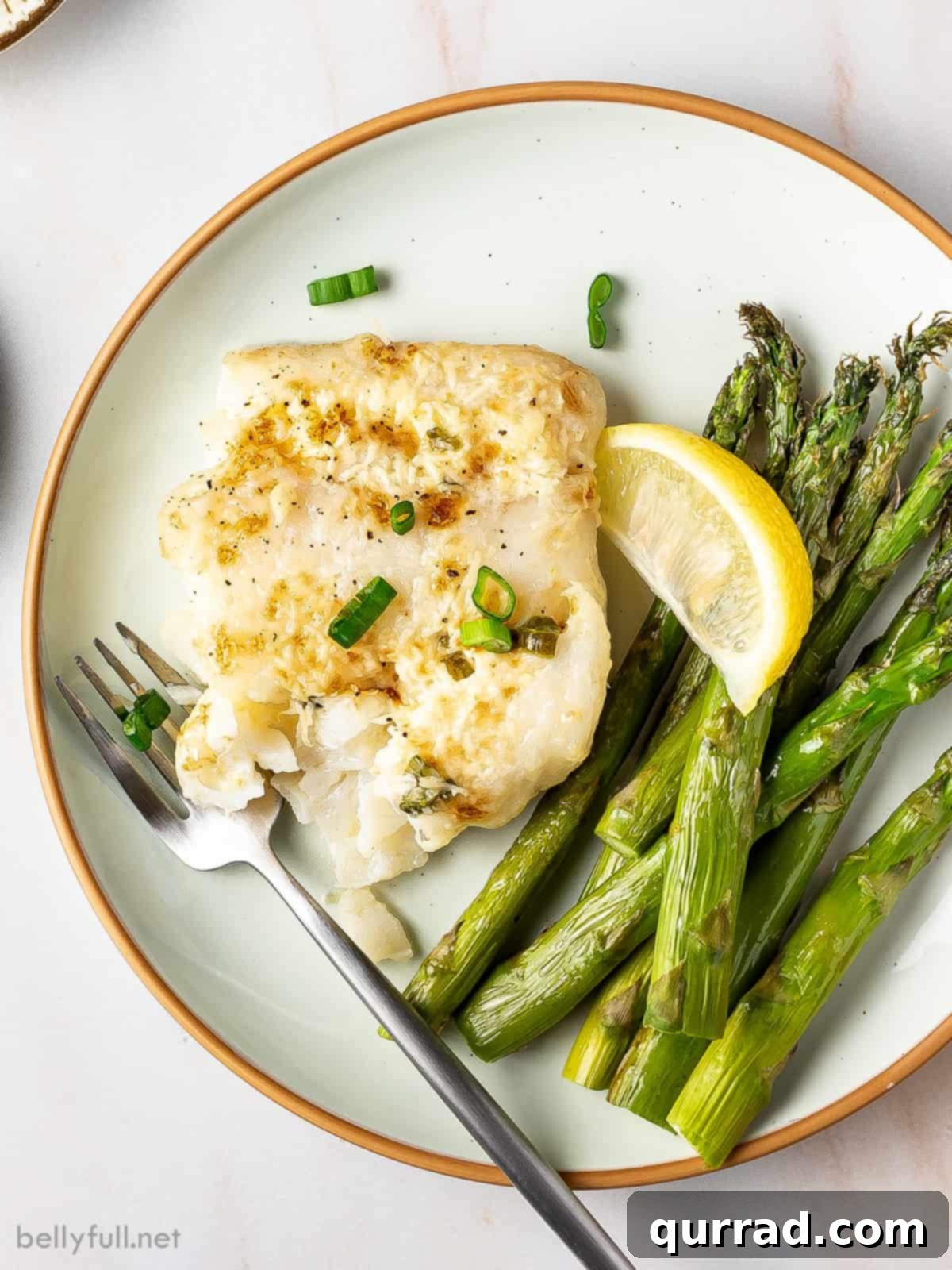 Overhead view of a beautifully plated serving of creamy baked halibut alongside steamed asparagus and a fresh lemon wedge.