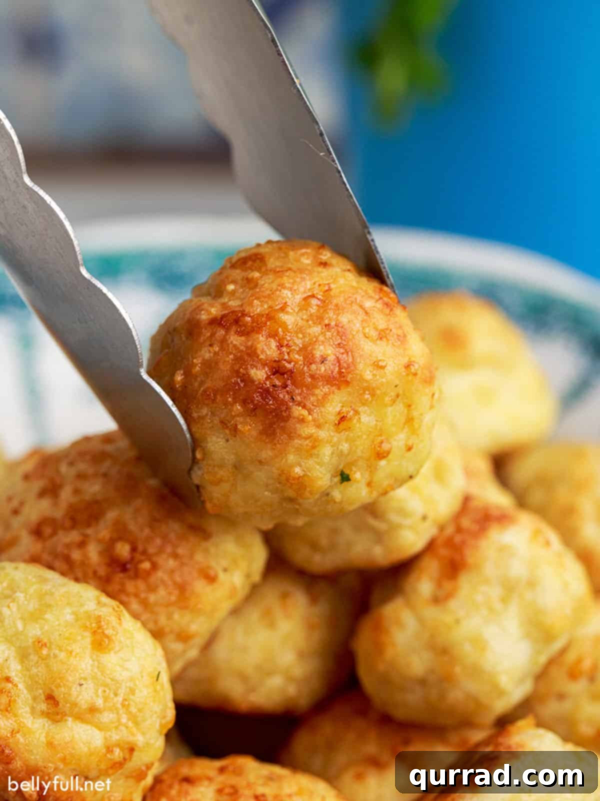 Savory Chicken Meatballs 4 Tongs placing a perfectly baked chicken meatball on top of a bowl filled with other golden brown meatballs.