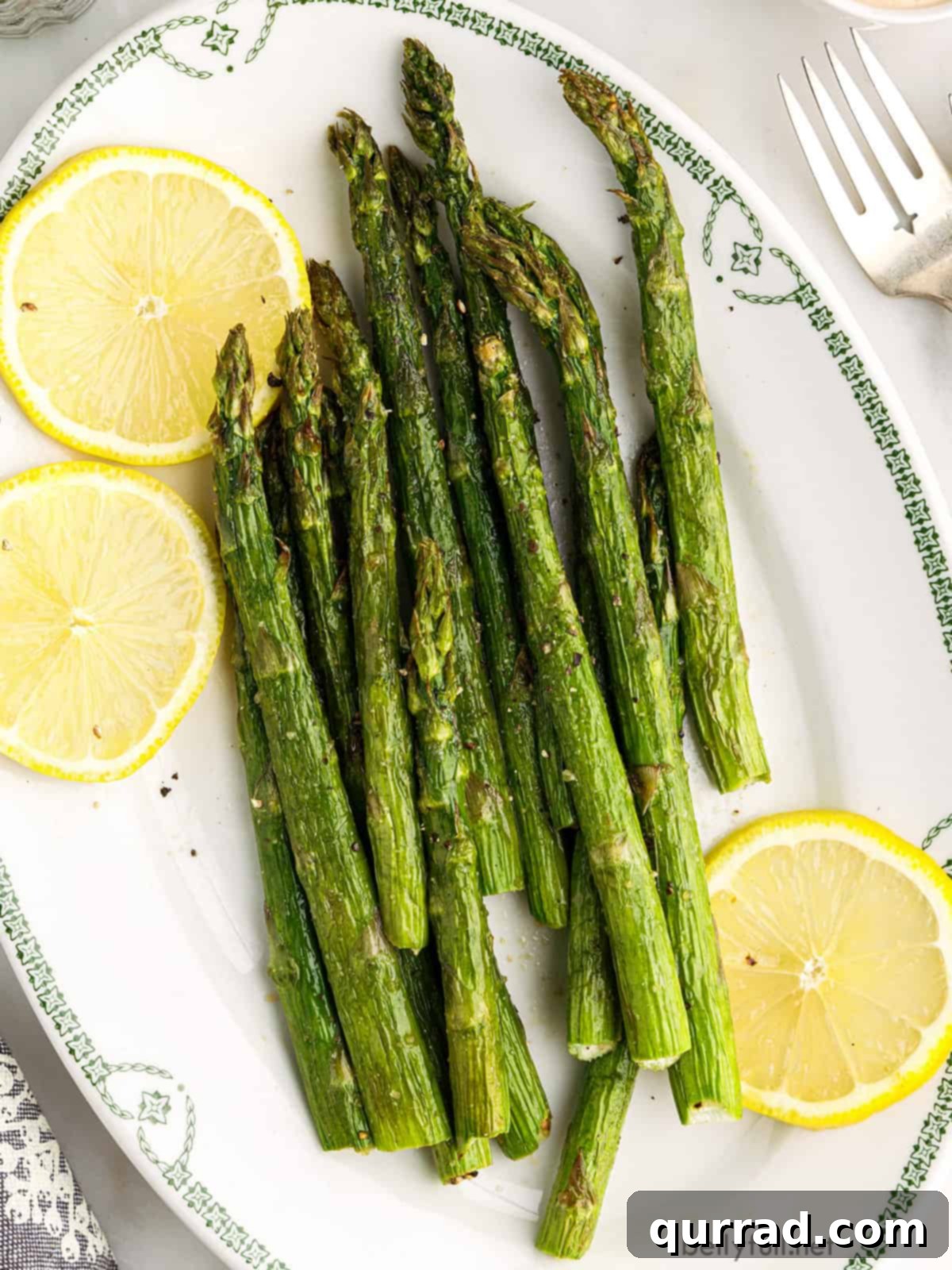 Crispy Air Fryer Asparagus 2 Overhead view of air fryer asparagus on a plate with lemon slices, garnished with parmesan