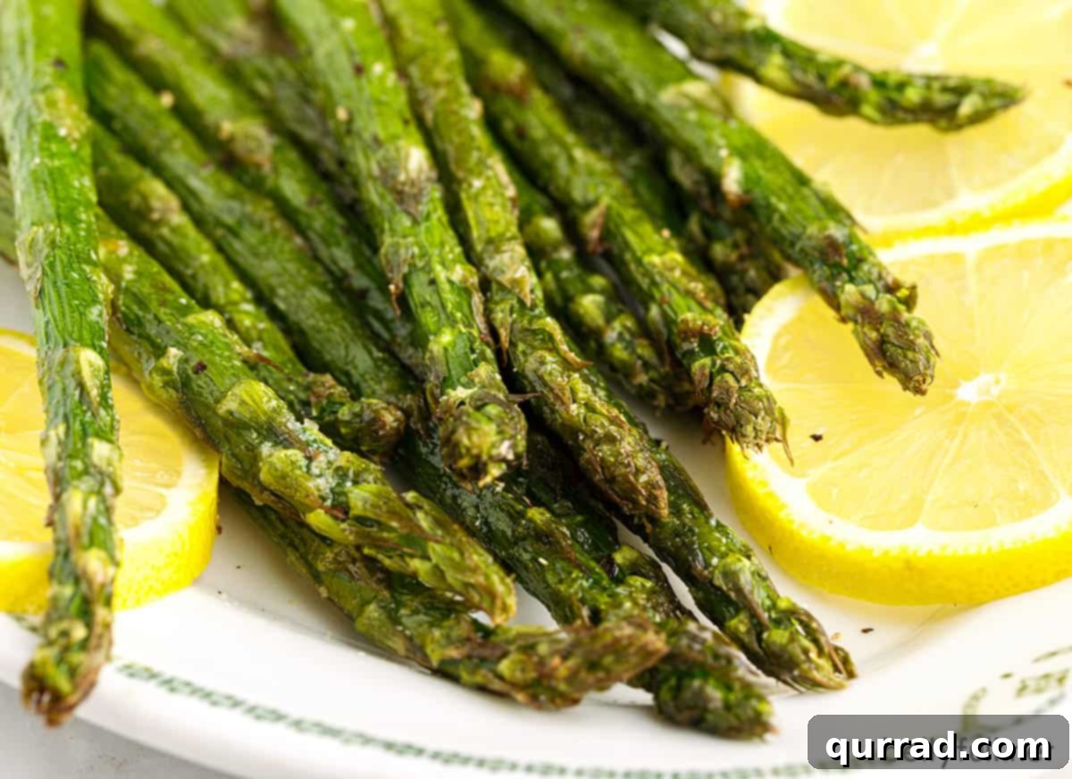 Crispy Air Fryer Asparagus 5 Close-up of air fryer asparagus on a plate with lemon slices and parmesan