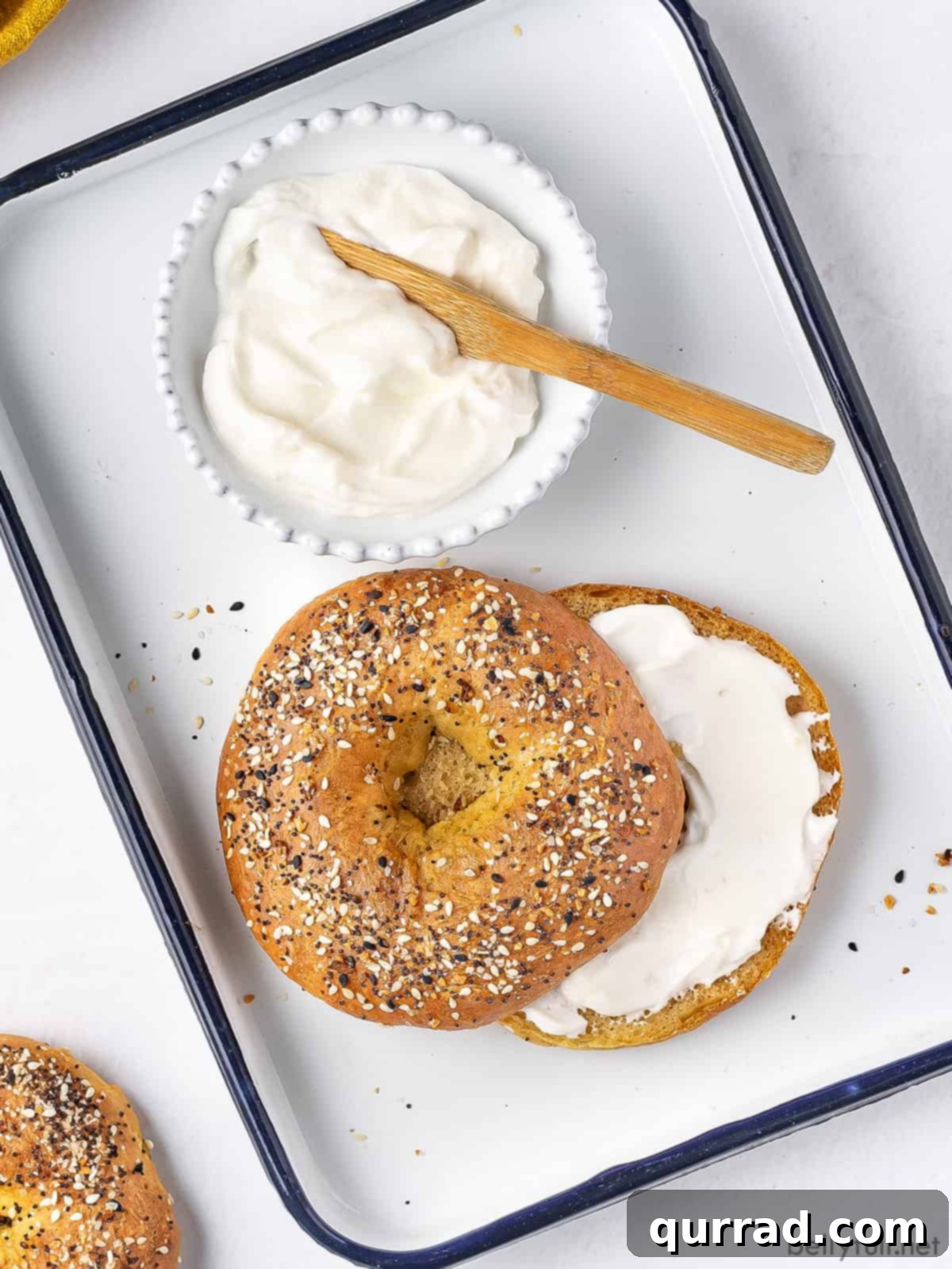 A freshly baked and sliced bagel with cream cheese, served on a tray, ready to eat.