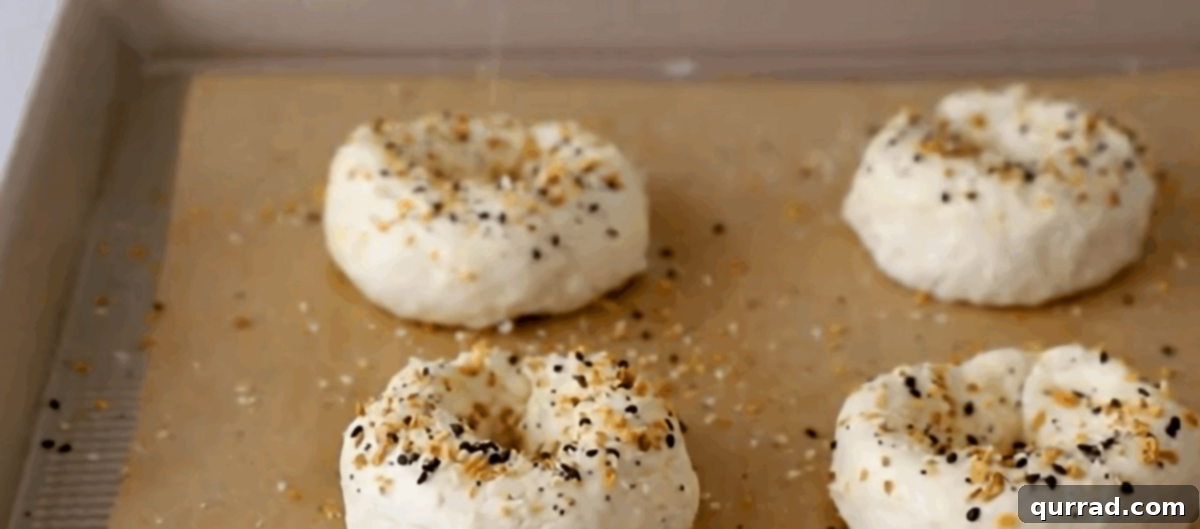 Four perfectly shaped bagels, brushed with egg wash and topped with everything bagel seasoning, ready for baking.