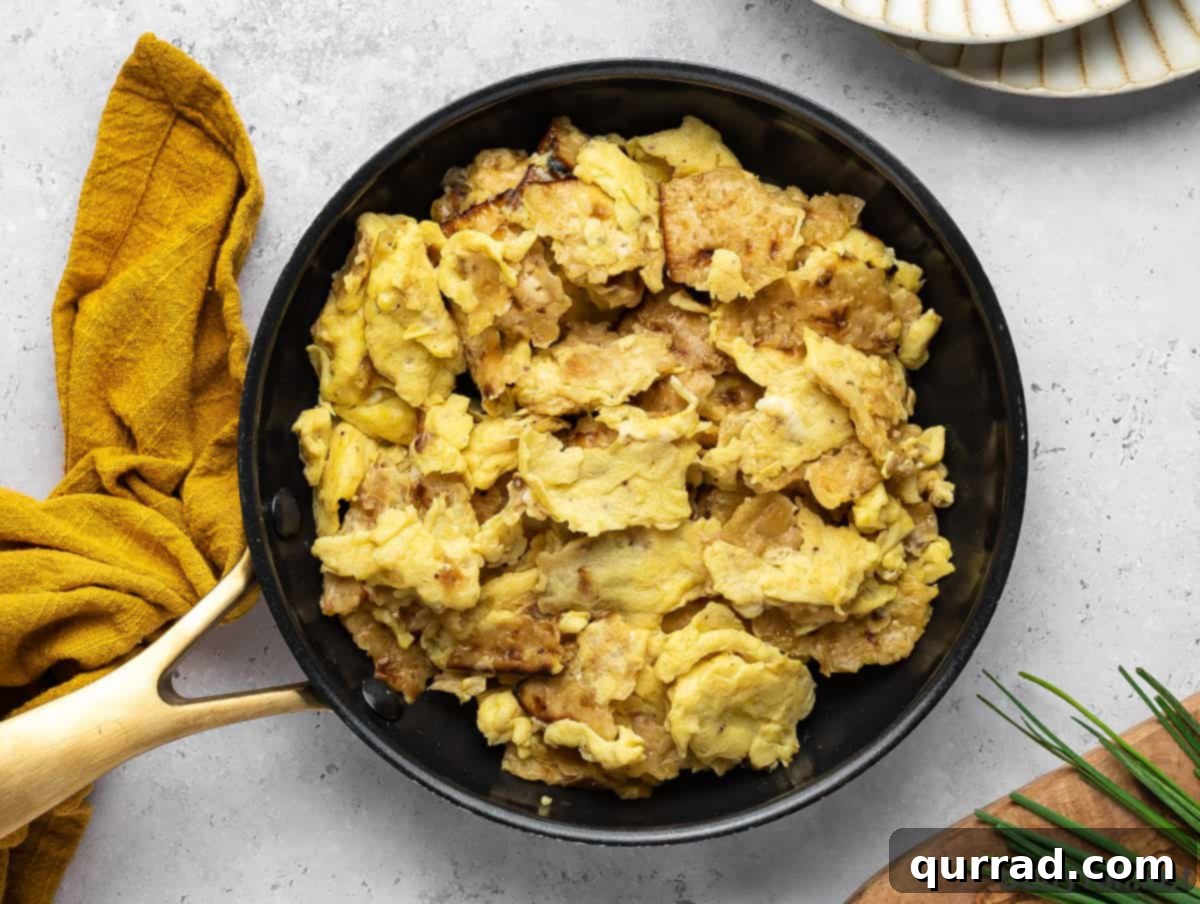 Overhead view of Matzo Brei being cooked in a fry pan, showing the matzo pieces mixing with scrambled eggs.