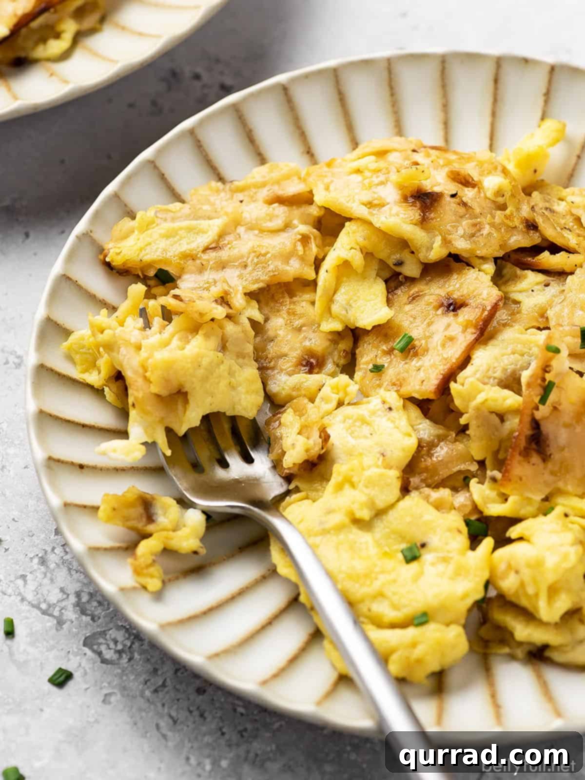 Scrambled eggs with crispy matzo pieces on a white plate with a fork, ready to eat.