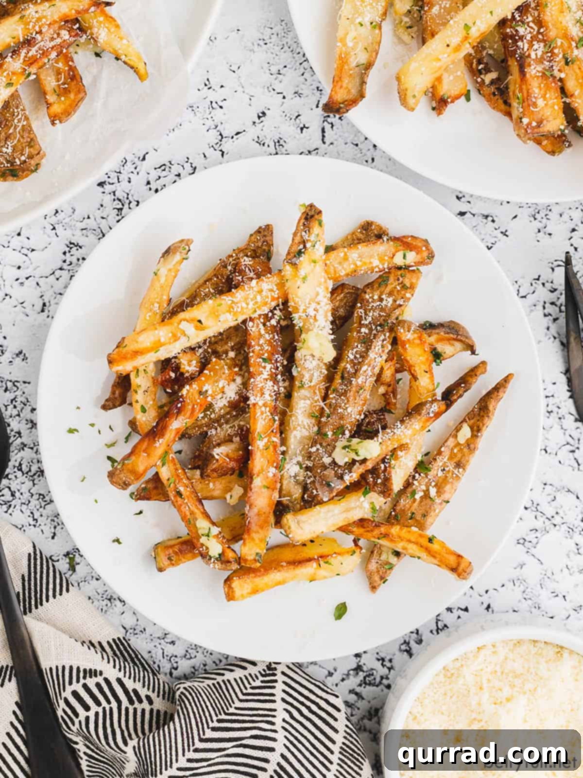 Overhead view of a white plate piled high with golden-brown garlic parmesan fries, garnished with fresh parsley.