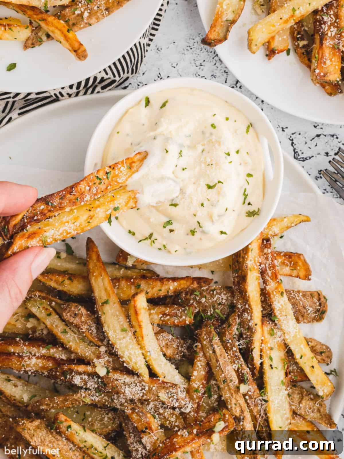A hand dipping a crispy air fryer french fry into a bowl of creamy aioli dipping sauce.