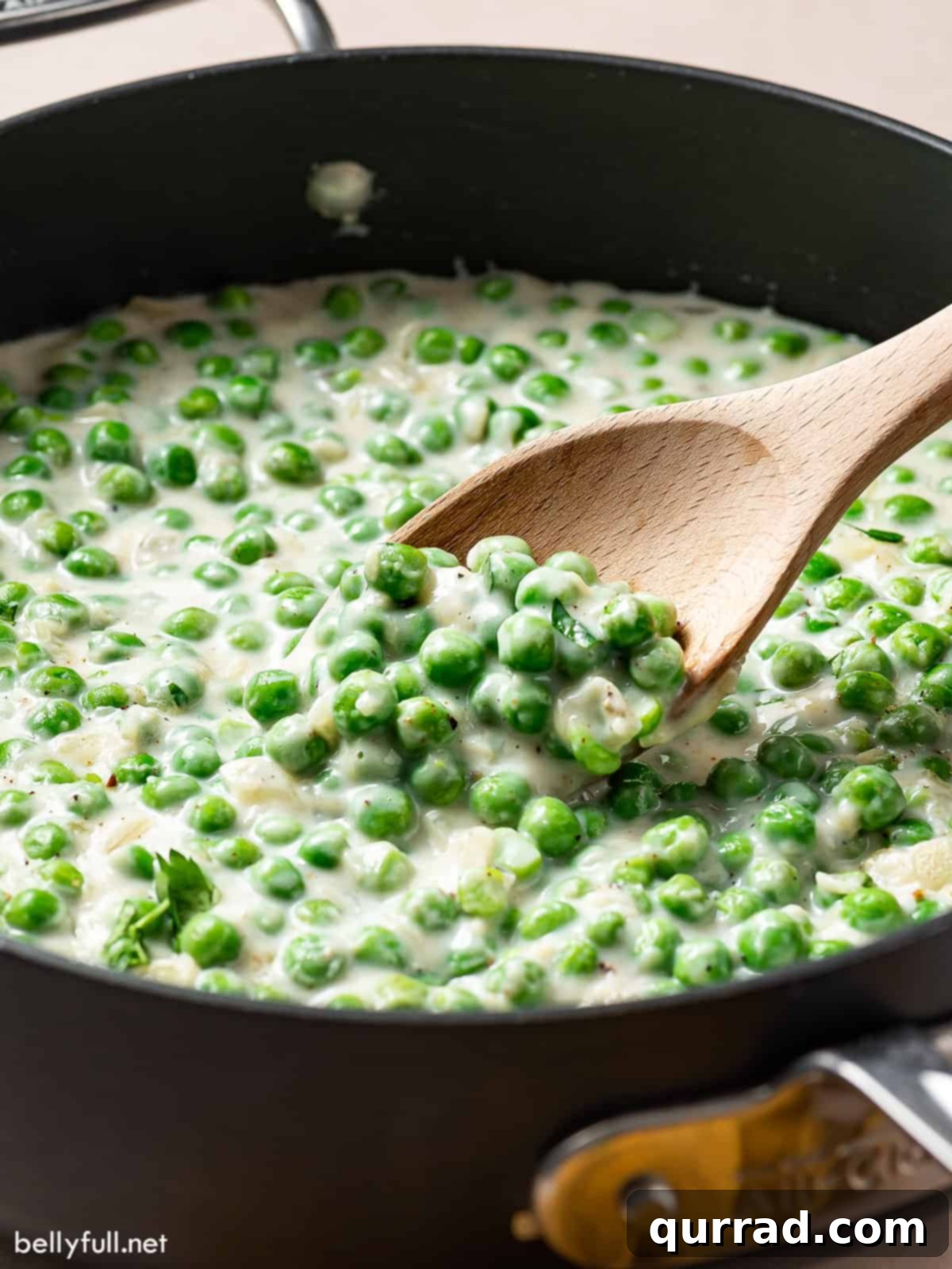 Creamy Braised Peas 2 Close up shot of creamy peas on a wooden spoon in a pan