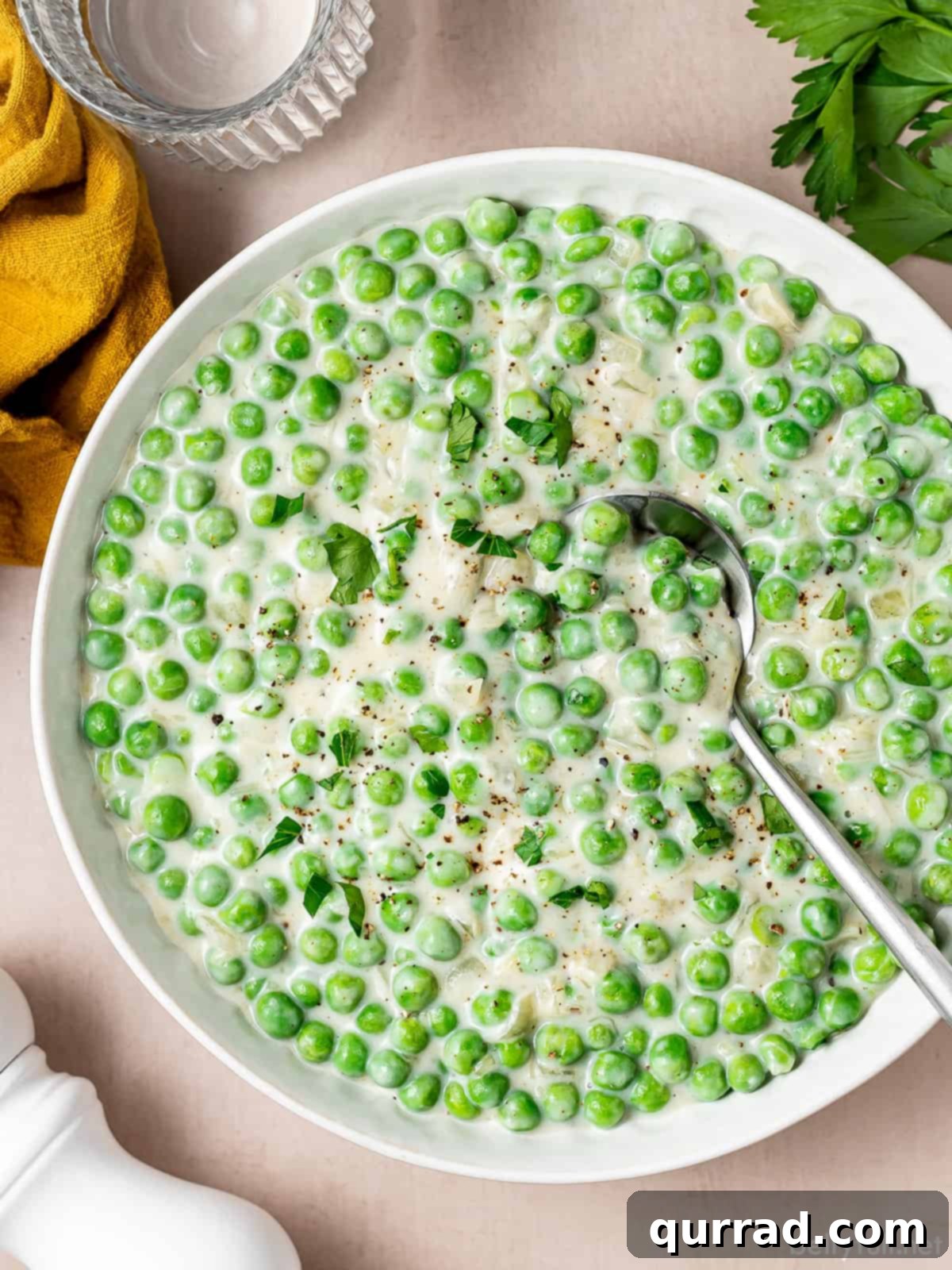 Creamy Braised Peas 4 Overhead shot of creamy peas in a white serving dish with a spoon