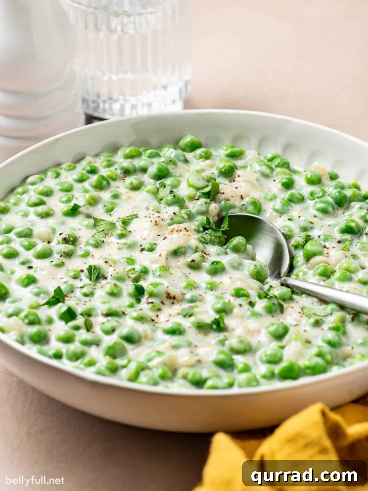 Creamy Braised Peas 5 Side angle view of creamy peas in a white serving bowl with a spoon