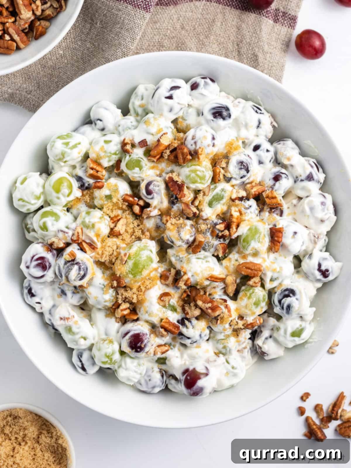 Overhead view of a bowl of creamy grape salad, garnished with pecans and brown sugar.