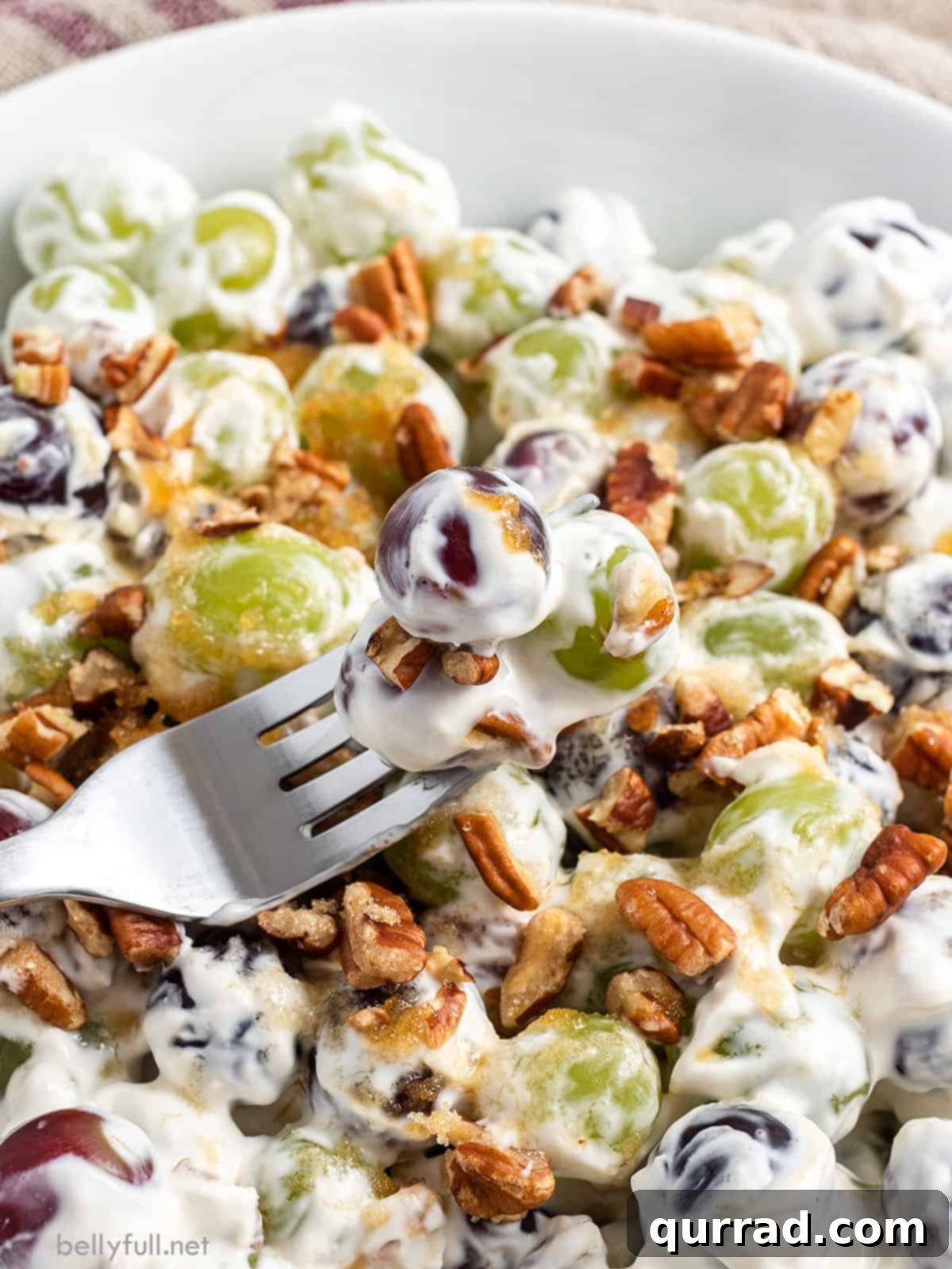 A fork with a bite of grape salad lifted from a bowl, showing the creamy texture and pecan topping.