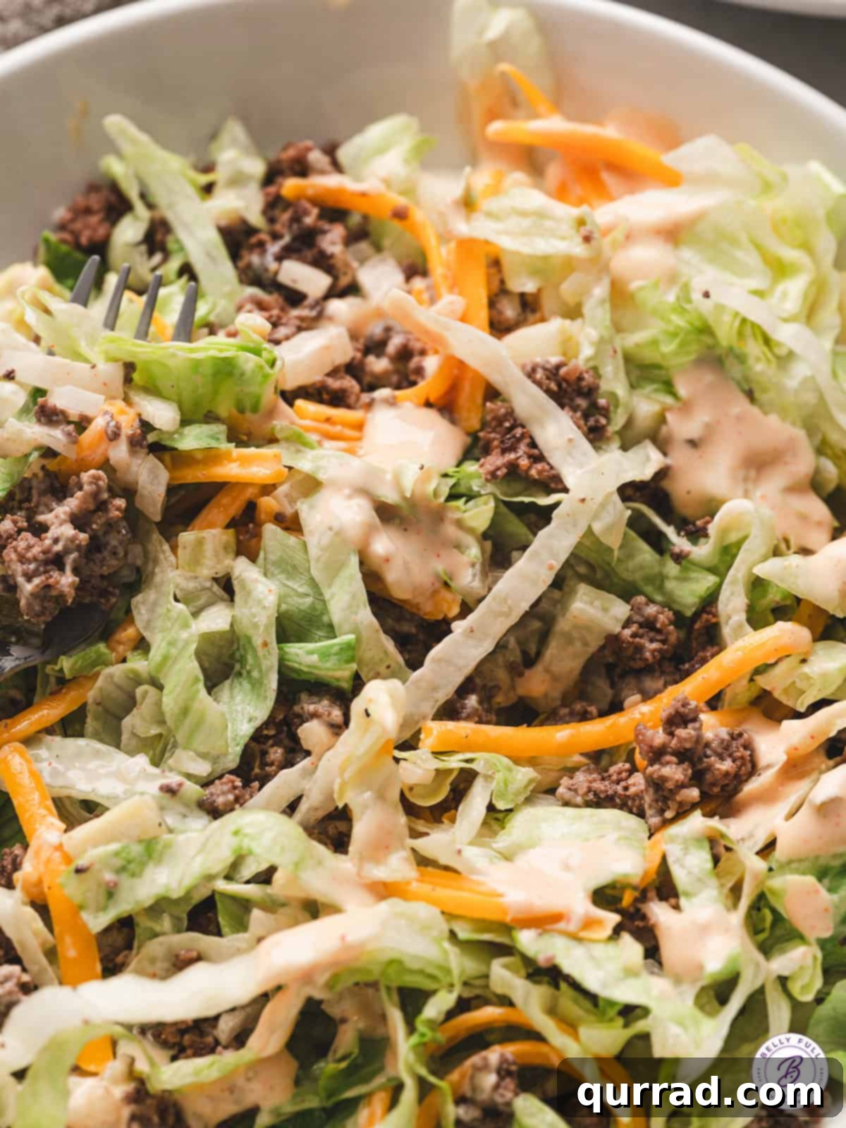 A beautifully presented Low Carb Big Mac Salad, showcasing all its components and the appetizing sauce, ready to be enjoyed.