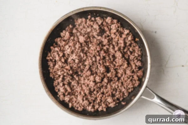 Cooked ground beef crumbles resting in a skillet after being browned and seasoned, ready for salad assembly.
