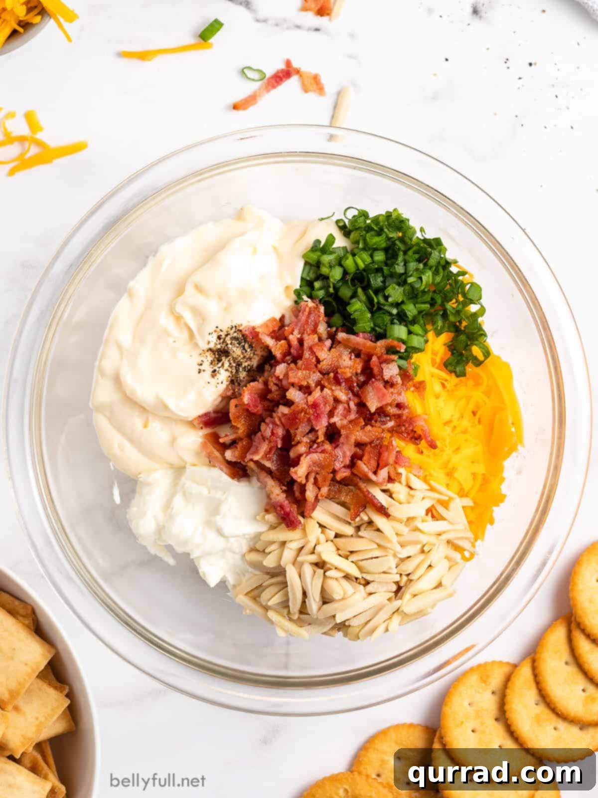 The Golden Delight 4 An overhead shot of all the Million Dollar Dip ingredients laid out on a wooden surface: a bowl of mayonnaise, crispy bacon bits, slivered almonds, shredded cheddar cheese, and chopped scallions, ready for mixing.