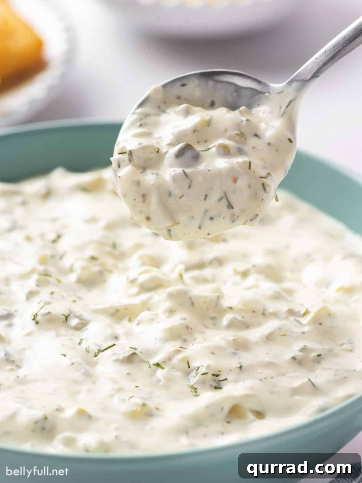 Zesty Fish Dip 4 A spoon overflowing with creamy homemade tartar sauce, held above a rustic bowl of more sauce