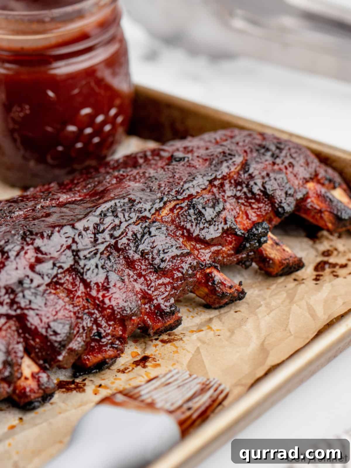 A rack of baby back ribs on a baking sheet, brushed with sauce, ready for the oven