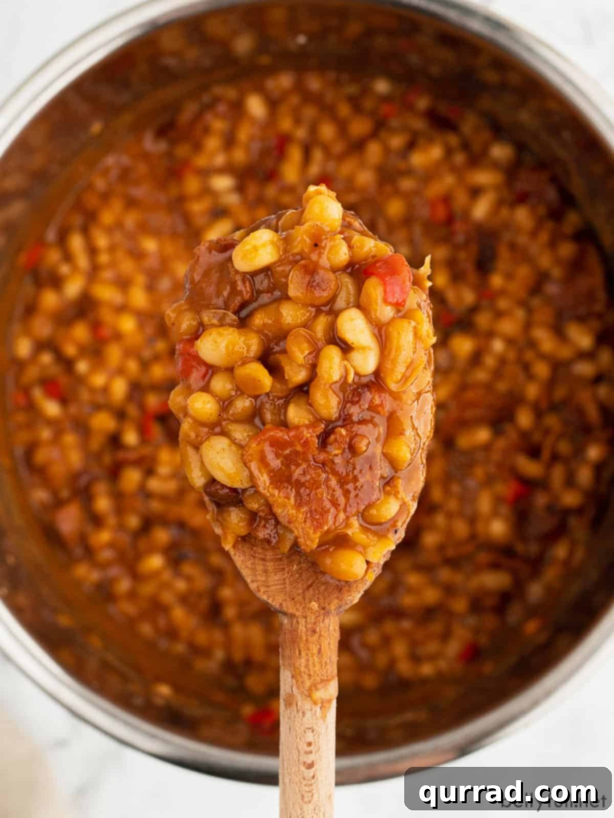 Instant Pot Baked Bean Magic 3 A spoonful of maple bacon baked beans being scooped from a serving bowl, with an Instant Pot in the background.