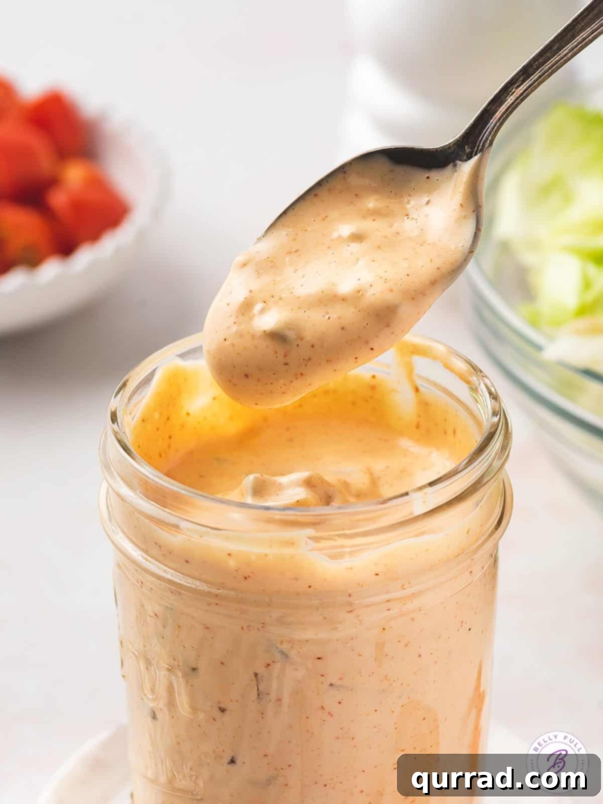A spoon hovering over a jar of homemade Thousand Island Dressing, ready to serve.