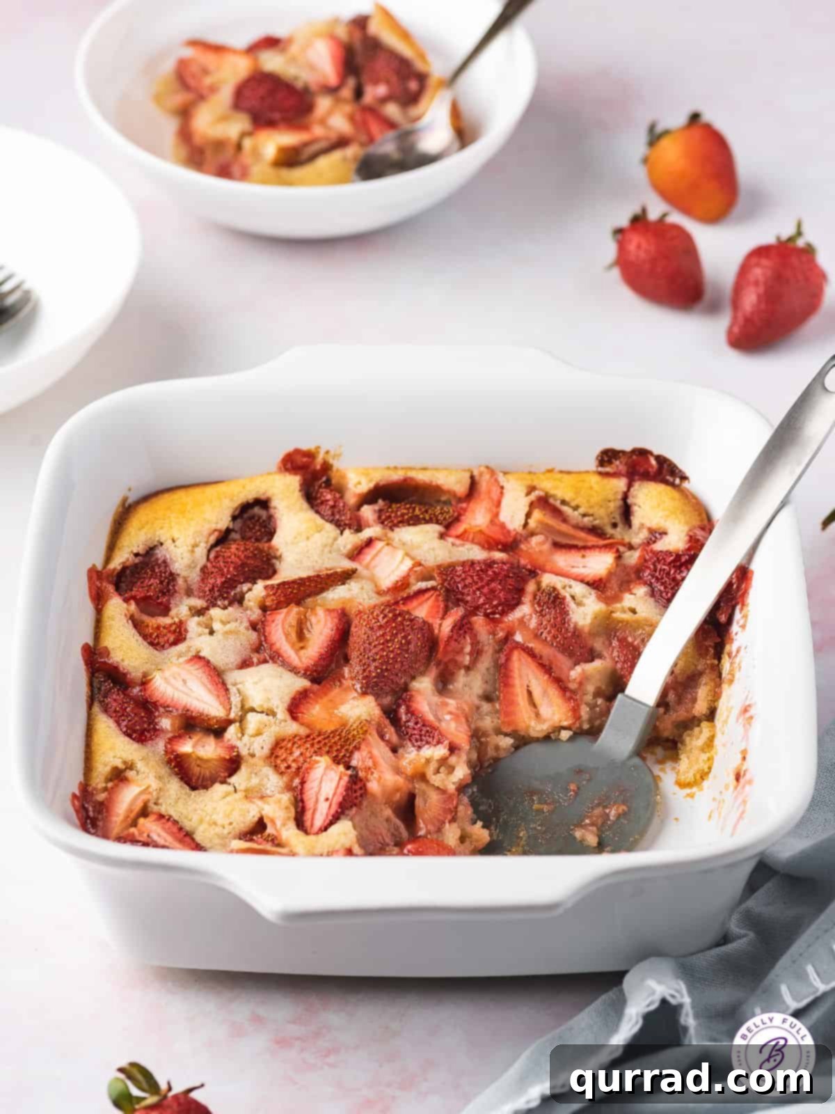 Sweet Summer Strawberry Cobbler 4 Close-up shot of a baked strawberry cobbler in a white baking dish with a serving spoon removing a portion