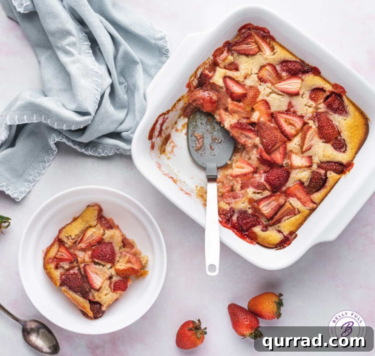 Sweet Summer Strawberry Cobbler 5 Overhead view of a baked strawberry cobbler in a white baking dish with a serving spoon inside, ready to be served