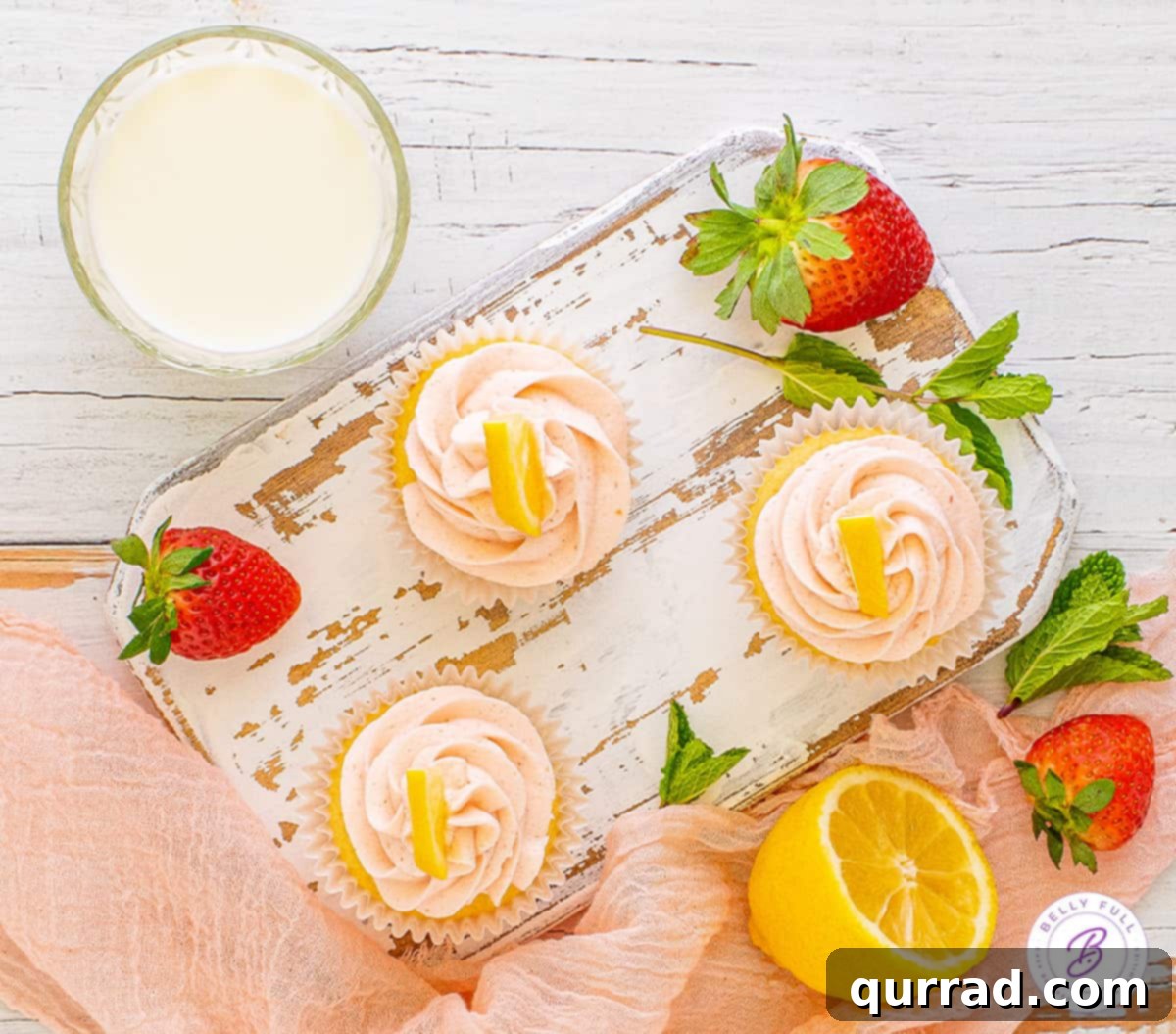 Bright Lemon Zing Cupcakes 3 An overhead view of three beautifully frosted lemon cupcakes with strawberry buttercream, arranged on a rustic wooden surface.