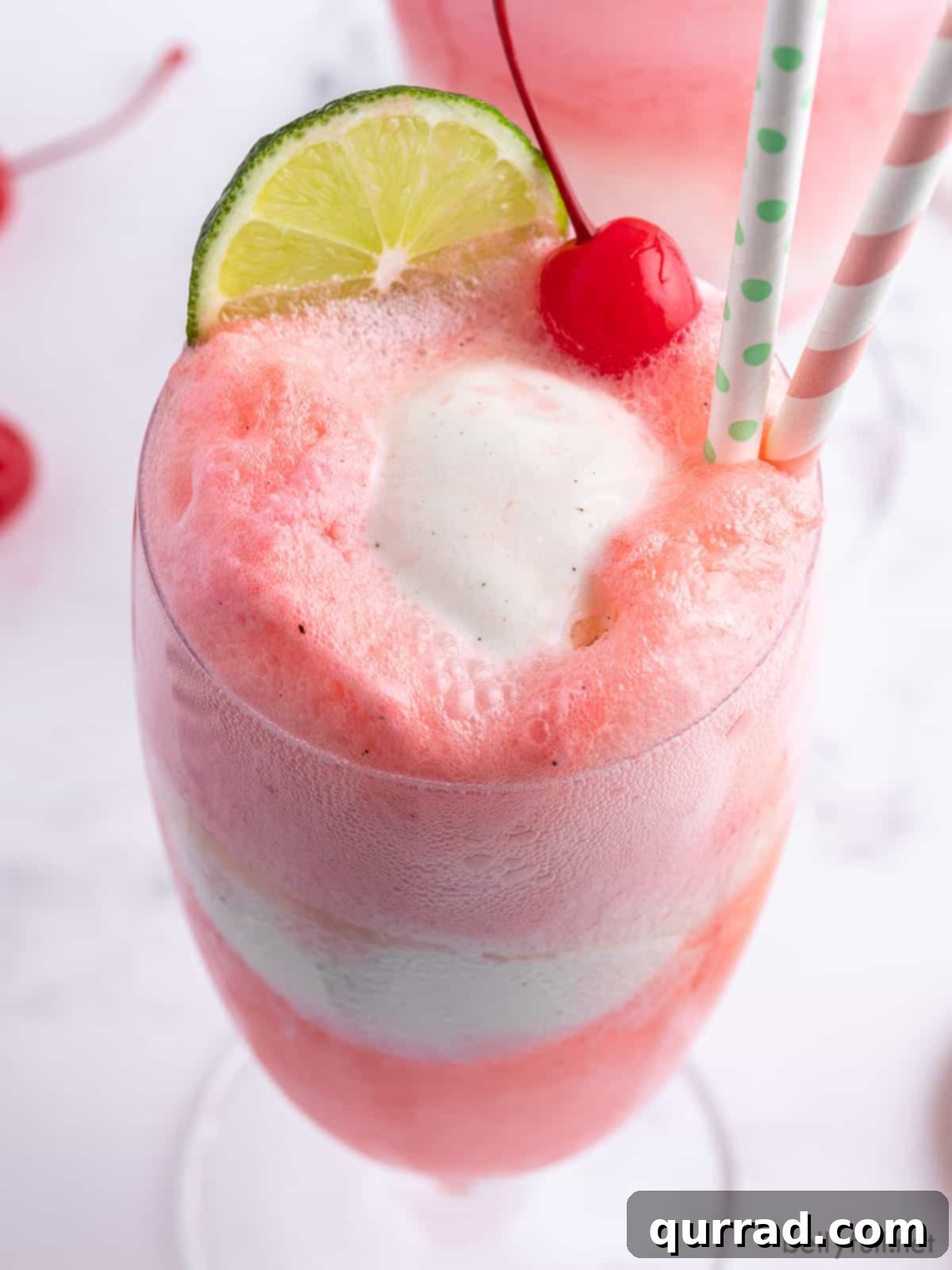 close up ice cream float with a maraschino cherry and lime wedge in a clear glass