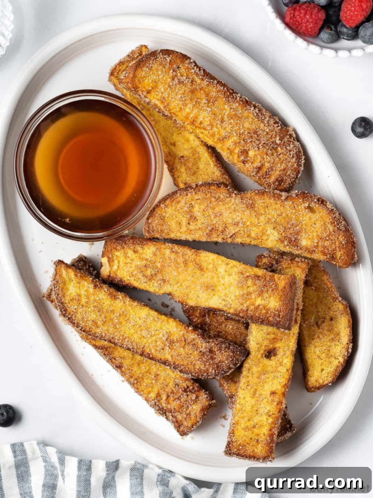 An overhead view of a rustic wooden platter laden with air fryer French toast sticks, accompanied by a small bowl of golden maple syrup, ready for dipping.
