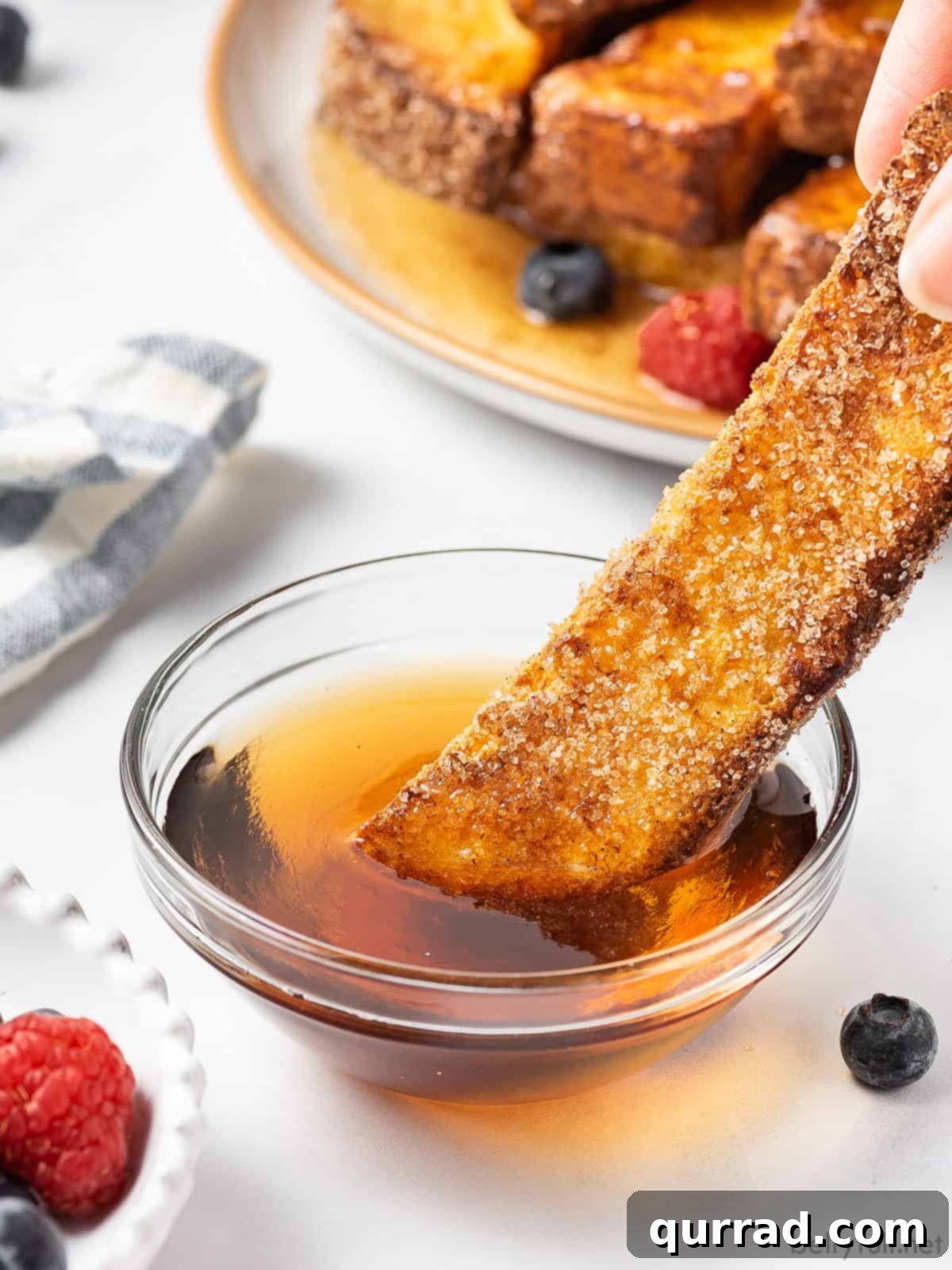 A close-up shot of a single air fryer French toast stick being dipped into a luscious pool of maple syrup, highlighting its perfectly golden-brown and crispy texture.