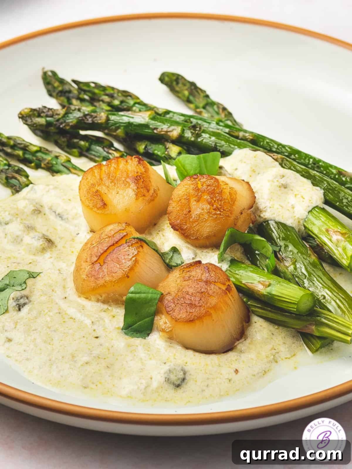 Angled view of a plate of scallops with pesto cream and asparagus, beautifully arranged for an elegant meal.