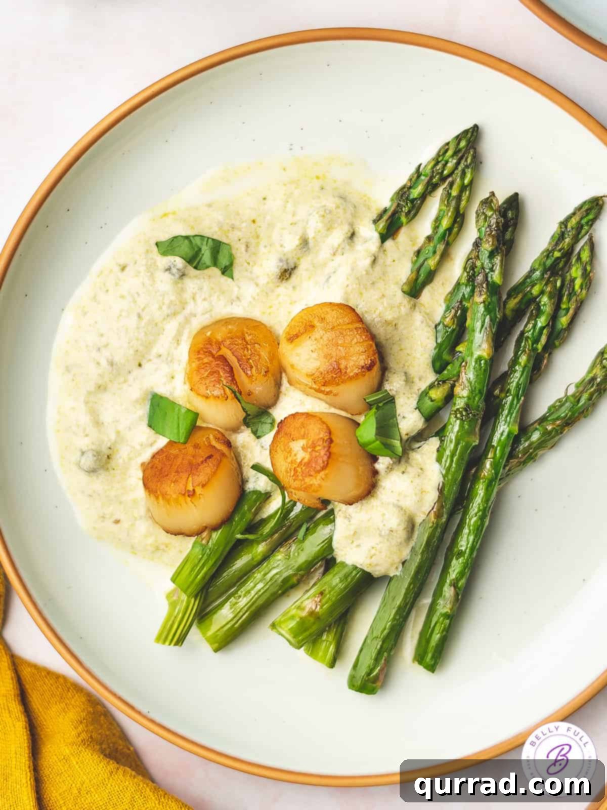 Overhead view of a perfectly plated dish of seared scallops with a generous swirl of pesto cream sauce.