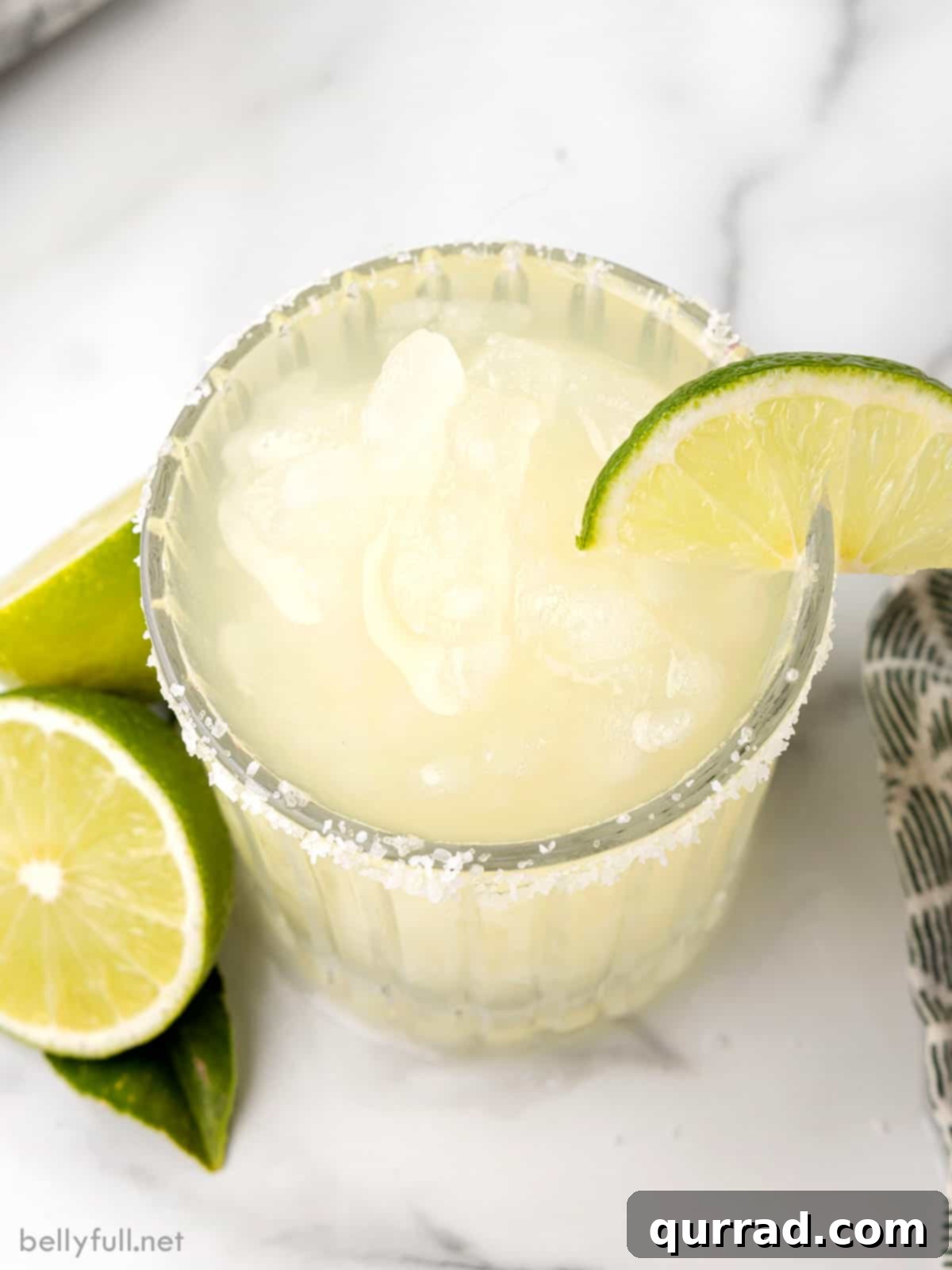 The Ideal Frozen Margarita: A Top-Down Perspective of Refreshment. The perfect frozen drink for summer pleasure. A pristine overhead shot showcasing a perfectly crafted frozen margarita in a classic glass, adorned with a neat salted rim and a fresh lime wedge, ready to be enjoyed.