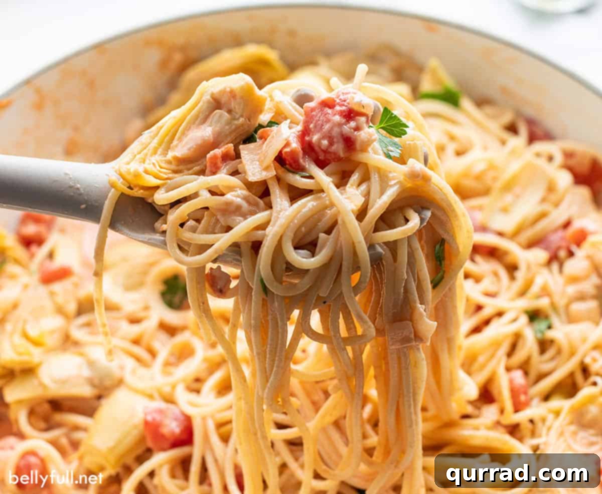 cream pasta with tomatoes and artichokes hanging from pasta ladle