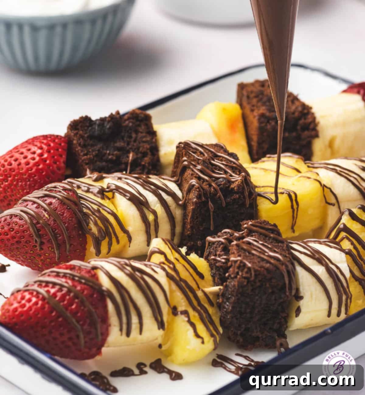 Fruity Banana Split Skewers 3 Close-up of a banana split dessert kabob featuring brownie, banana, pineapple, and strawberry, generously drizzled with chocolate.
