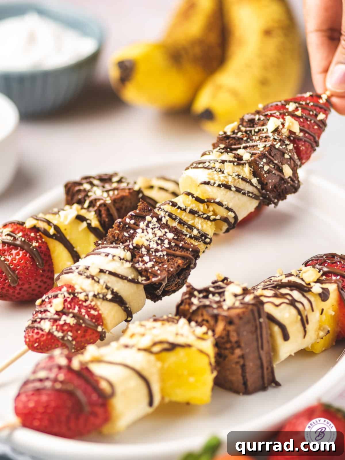 Fruity Banana Split Skewers 5 A banana split dessert kabob, generously garnished with finely chopped nuts and chocolate drizzle, ready for serving.