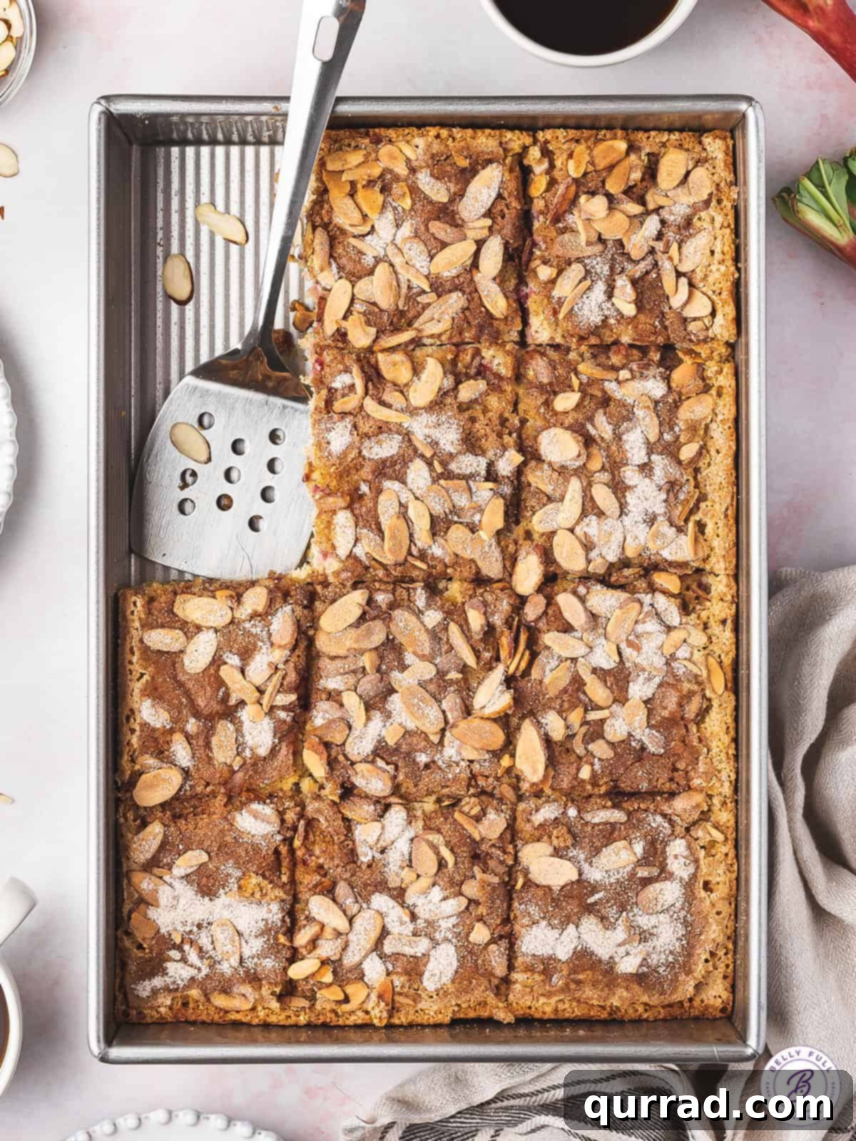 The complete Rhubarb Coffee Cake with Almonds, perfect for sharing or enjoying over several days. Overhead shot of a full rhubarb coffee cake with two slices already removed, showing the moist interior texture and distribution of rhubarb pieces.