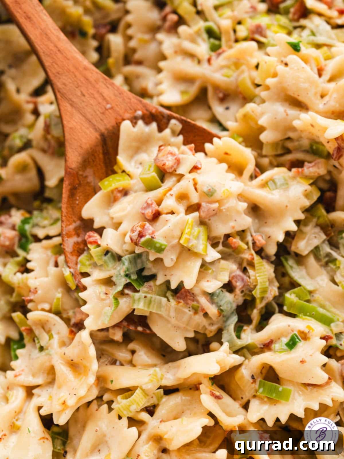 creamy bowtie pasta with pancetta and onion on wooden spoon