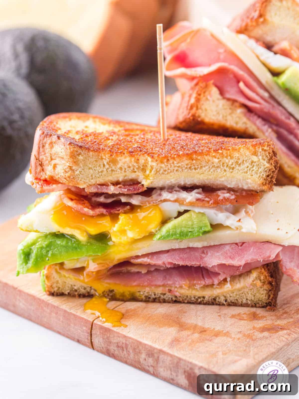 The Ultimate BEACH Sandwich: Bacon, Egg, Avocado, Cheese, Ham A ham and cheese sandwich with avocado, bacon, and egg on brioche bread, showcasing layers of delicious ingredients.