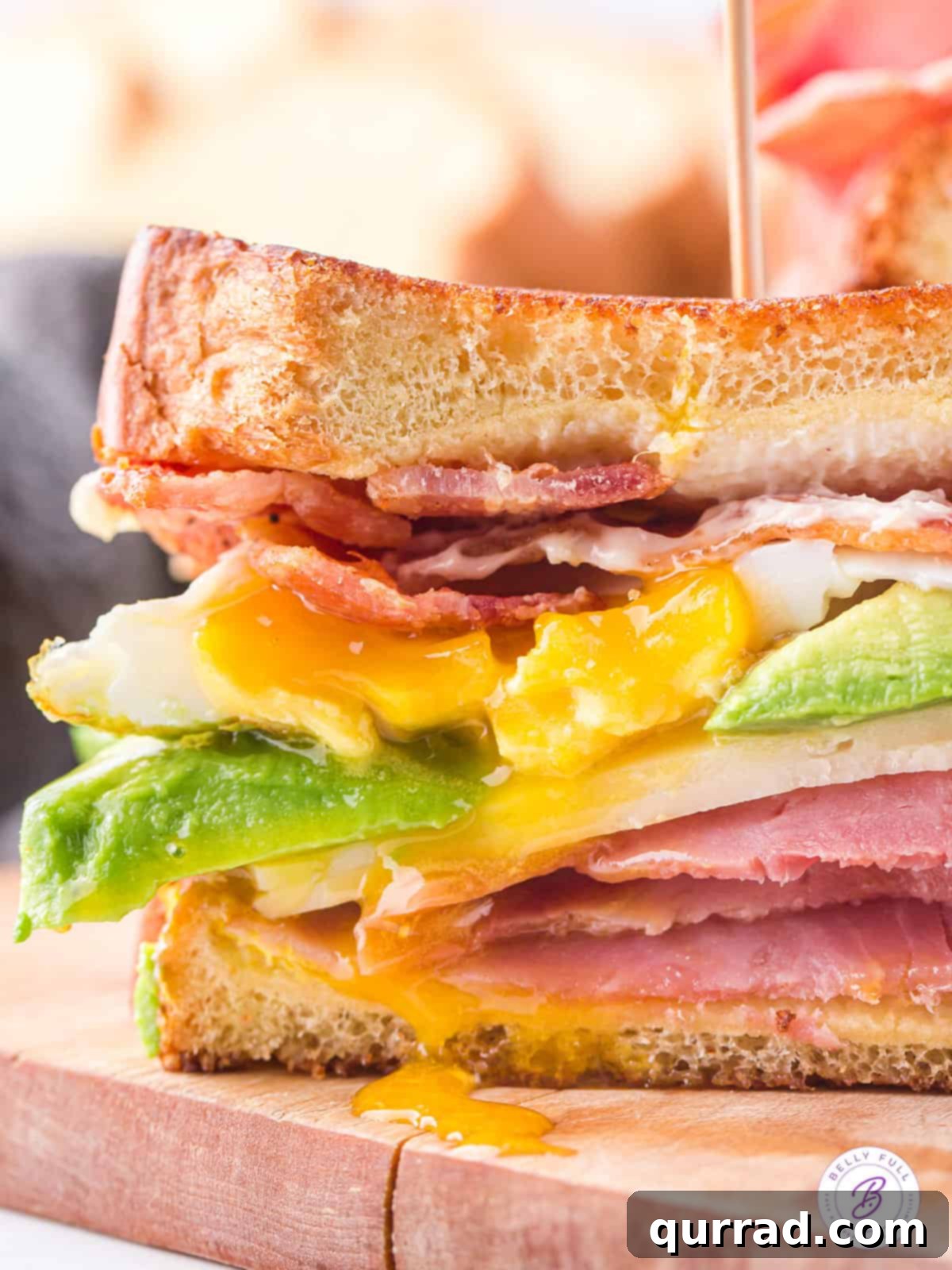 BEACH Sandwich: A Stack of Savory Goodness Side view of a perfectly layered BEACH sandwich, showcasing the generous fillings of bacon, egg, avocado, cheese, and ham.