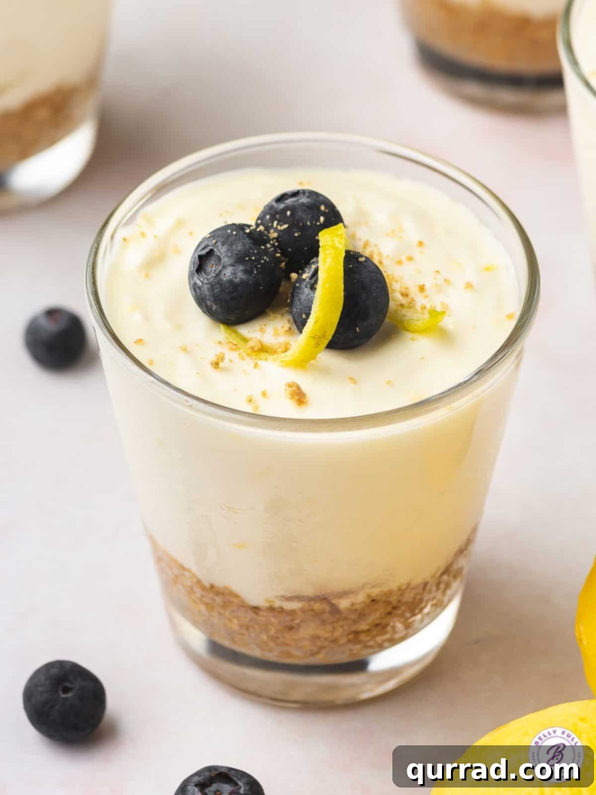 Experience the light and creamy texture of this Lemon Cheesecake Mousse, a refreshing no-bake spring and summer dessert! Overhead angled view of a vibrant lemon cheesecake mousse in a glass cup, garnished with a lemon slice and a blueberry.