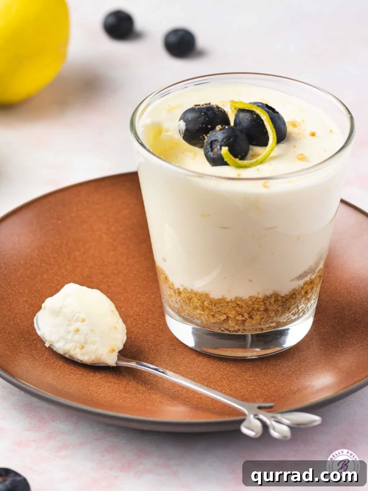 Savor the light and creamy texture of this Lemon Cheesecake Mousse, a delightful no-bake treat for spring and summer! A single serving of lemon cheesecake mousse in a glass, resting on a small white plate next to a spoon, ready to be enjoyed.