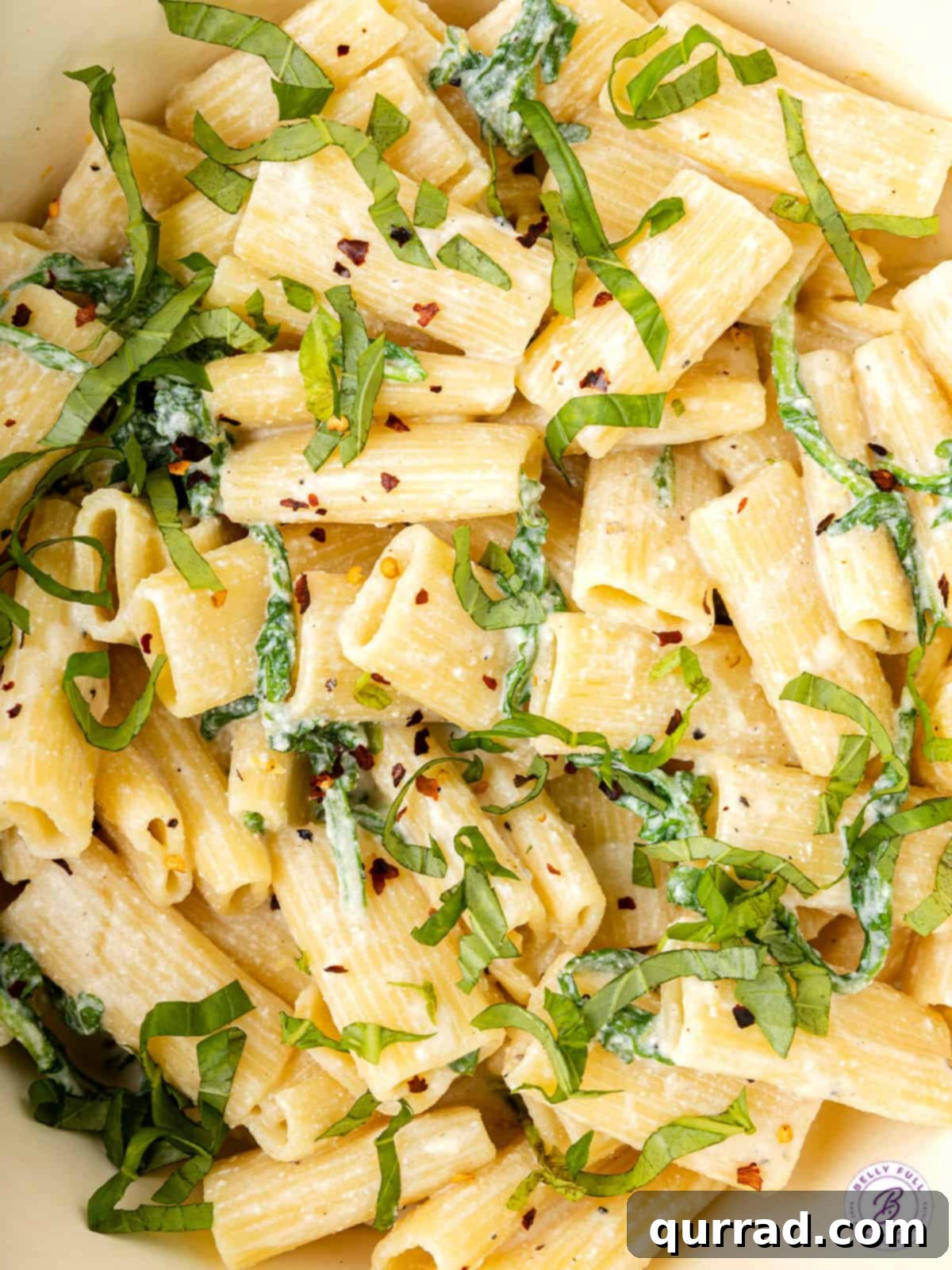 close rigatoni pasta with cream sauce and julienned basil