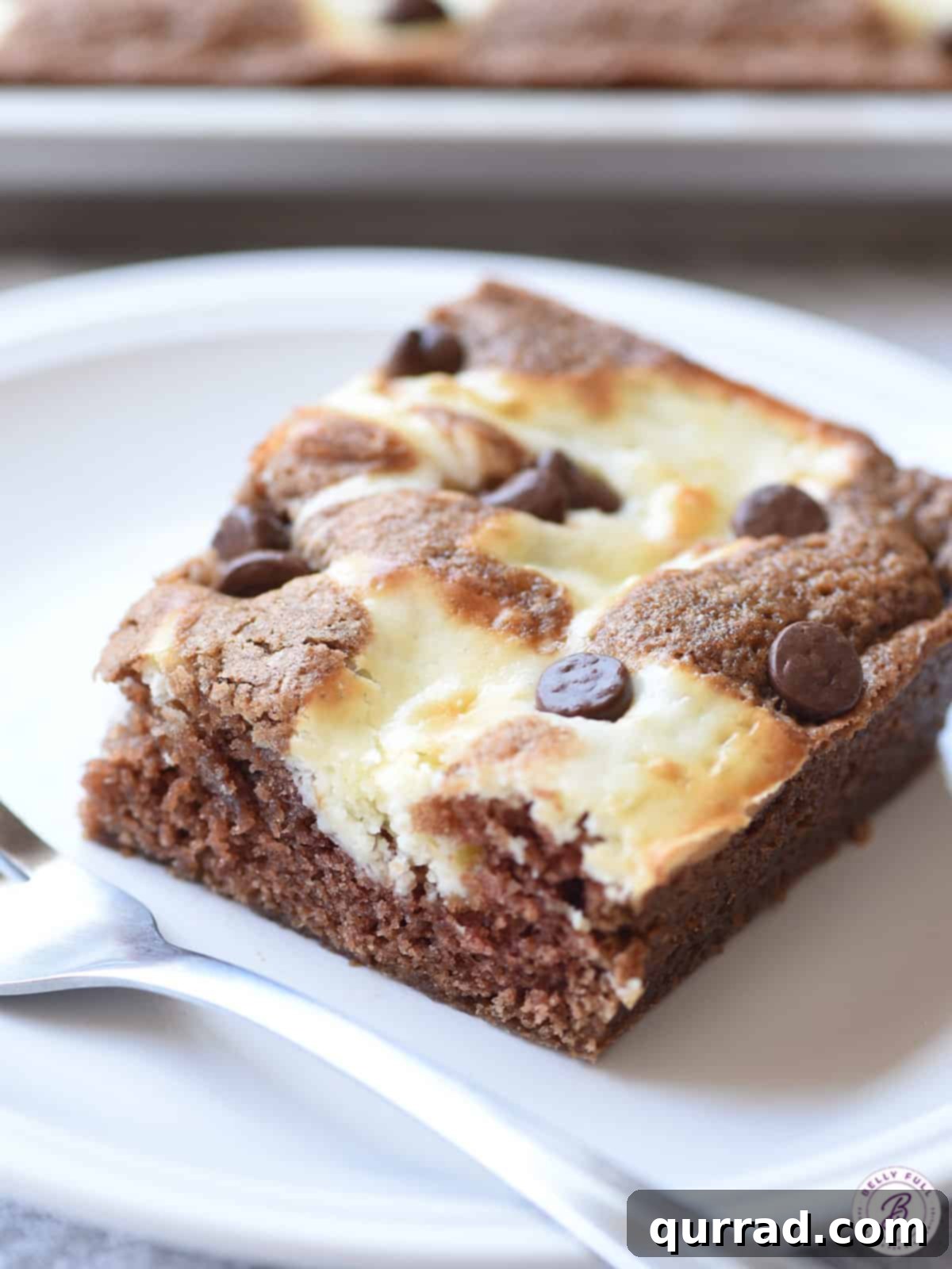 Our perfect Cheesecake Marble Square, ready for its close-up. A single marble cheesecake square placed delicately on a plate with a fork, ready to be enjoyed.