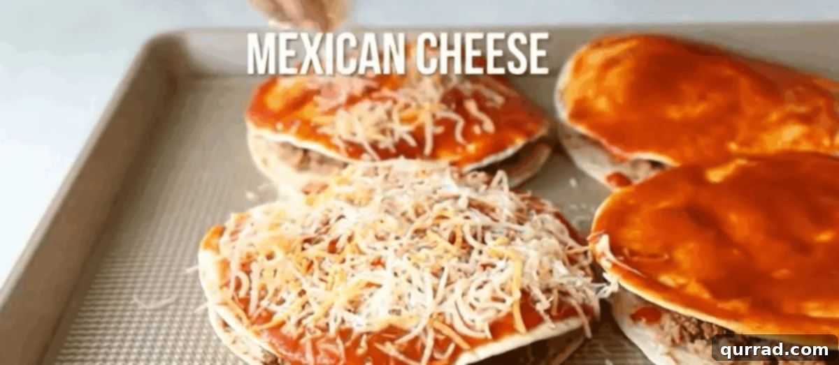 Tortillas stuffed with meat and beans being topped with sauce and cheese. 