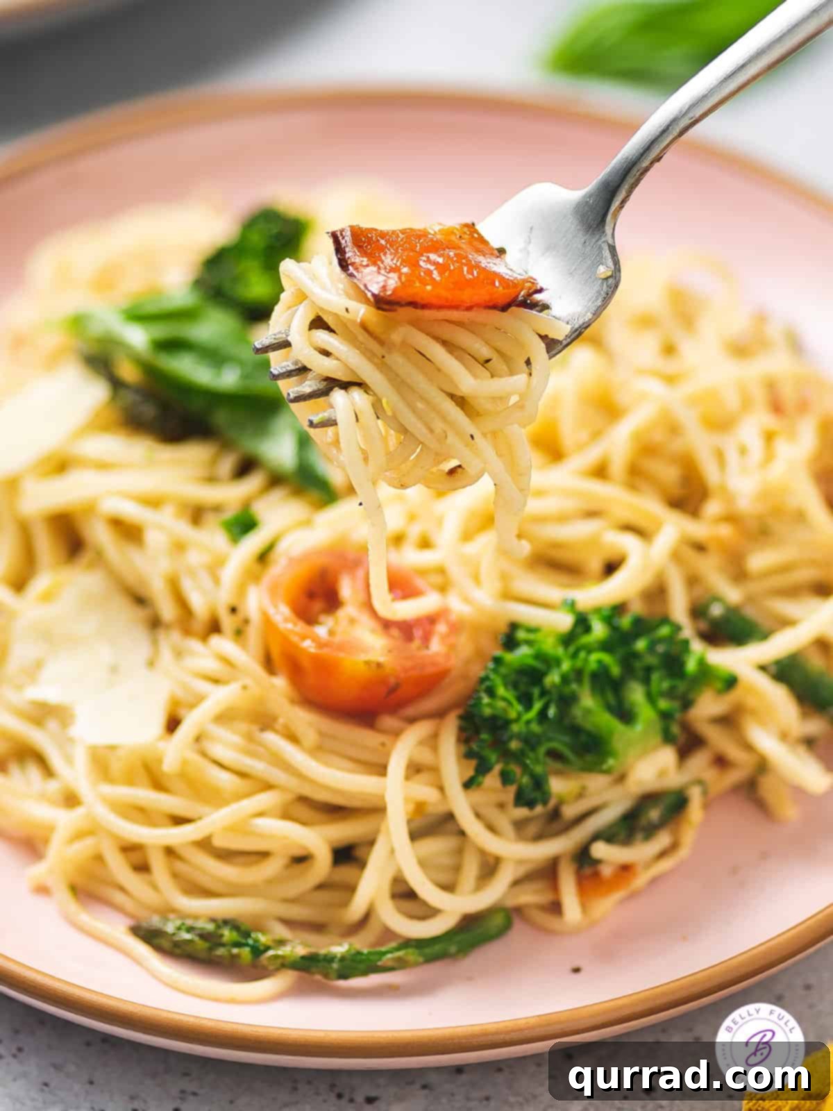 Loaded with fresh veggies like broccoli and asparagus and a lemon cream sauce, Pasta Primavera is a quick and easy dinner recipe. A fork holding a twirl of pasta above a full plate of vibrant pasta primavera, showcasing its freshness.