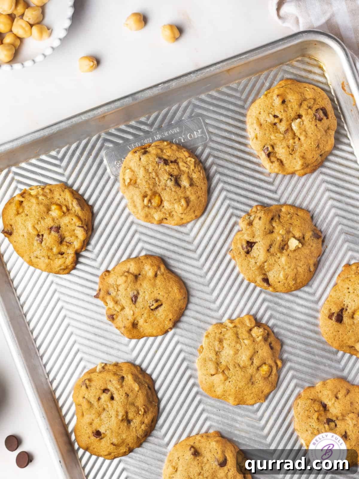 These Chickpea Cookies with Chocolate Chips are super easy to make (no chilling required!) and packed with protein! Close-up shot of baked chickpea chocolate chip cookies on a parchment-lined baking sheet, showcasing their texture.