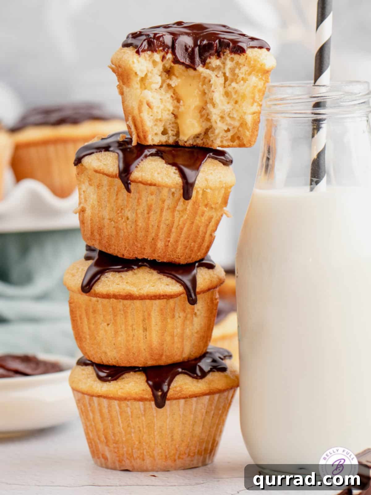 Boston Cream Pie cupcakes artfully arranged next to a glass of milk, a perfect snack. A stack of Boston Cream Pie cupcakes next to a refreshing glass of milk, highlighting their deliciousness
