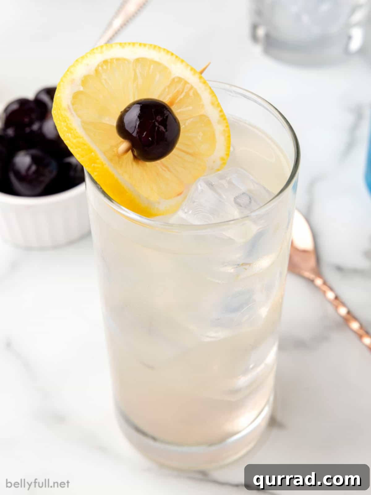 Tom Collins Cocktail: Angled View with Garnish An elegantly angled shot of a Tom Collins cocktail, featuring a clear glass with ice, lemon, and a cherry against a subtle background.