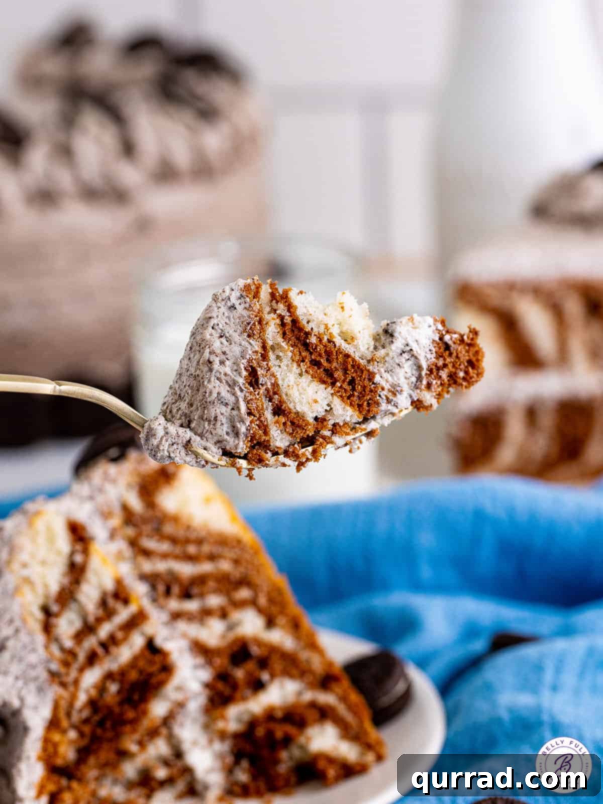 Experience the delightful taste and texture of this simple yet elegant Zebra Cake. A close-up shot of a fork taking a bite from a slice of zebra cake, clearly showing the alternating vanilla and chocolate layers, with creamy cookies and cream frosting.