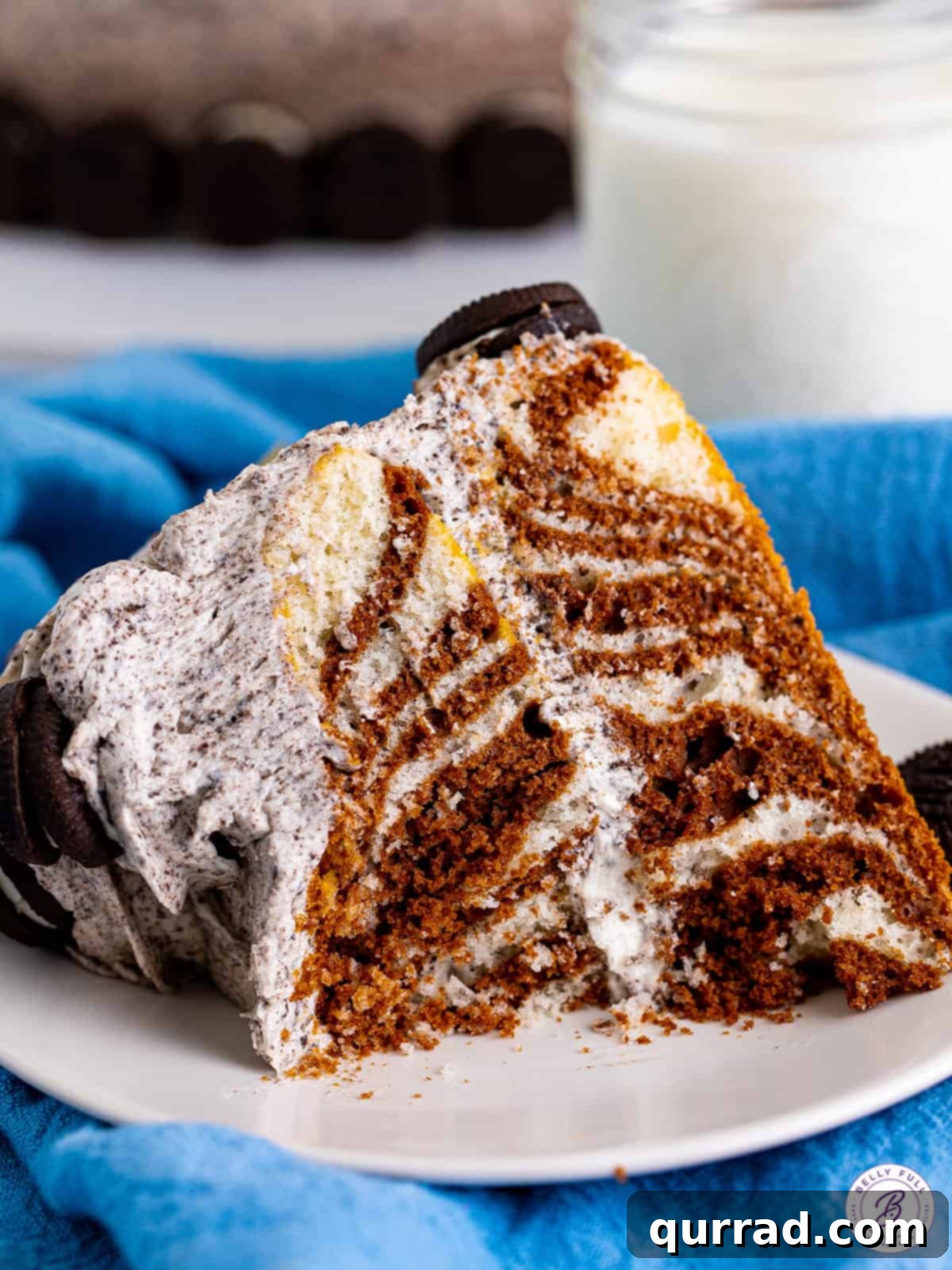 Indulge in a slice of this easy-to-make Zebra Cake, a perfect blend of flavor and striking design. A perfect slice of zebra cake on a white plate, with a small bite taken, highlighting the contrasting vanilla and chocolate layers and the creamy frosting.